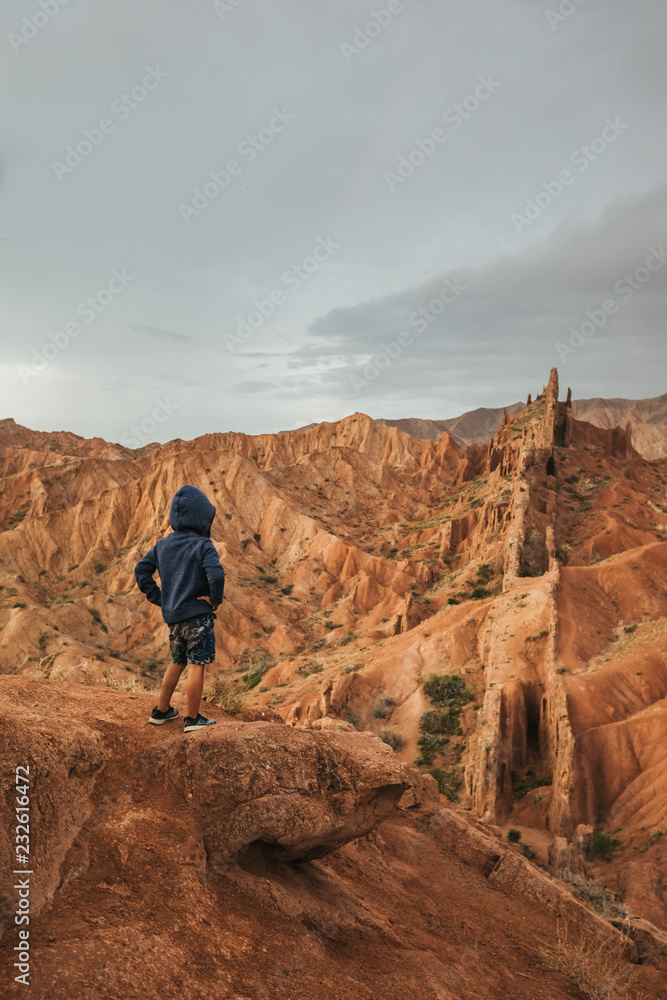 little boy standing in rugged bizzare mountain landscape, kyrgyzstan little boy standing in rugged bizzare mountain landscape, kyrgyzstan
