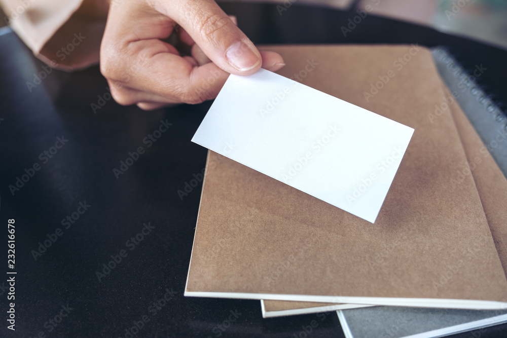 Obraz premium A businessman's hand holding and giving empty business card with notebooks on table
