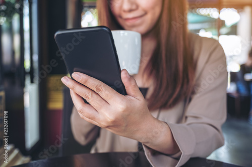 Closeup image of a beautiful Asian woman holding , using and looking at smart phone while drinking coffee in cafe