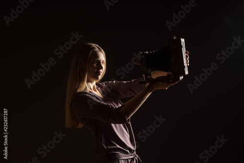 Caucasian white female model portrait. Beautiful girl, long blonde hair taking a picture with the camera. Woman posing studio shot on a black background © Artenex