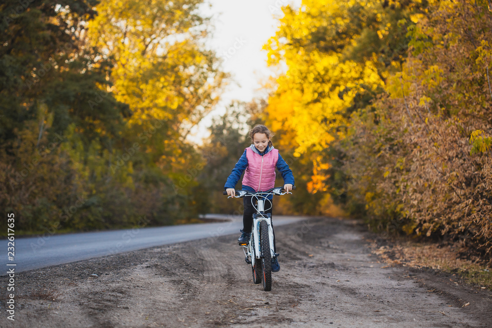 girl on a bicycle in the sunny autumn forest. happy girl cycling outdoors