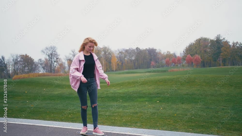 Young pretty beautiful blond hipster woman in pink windstopper having fun riding skateboard longboard downhill on beautiful road in slow motion Young pretty beautiful blond hipster woman in pink windstopper having fun riding skateboard longboard downhill on beautiful road in slow motion