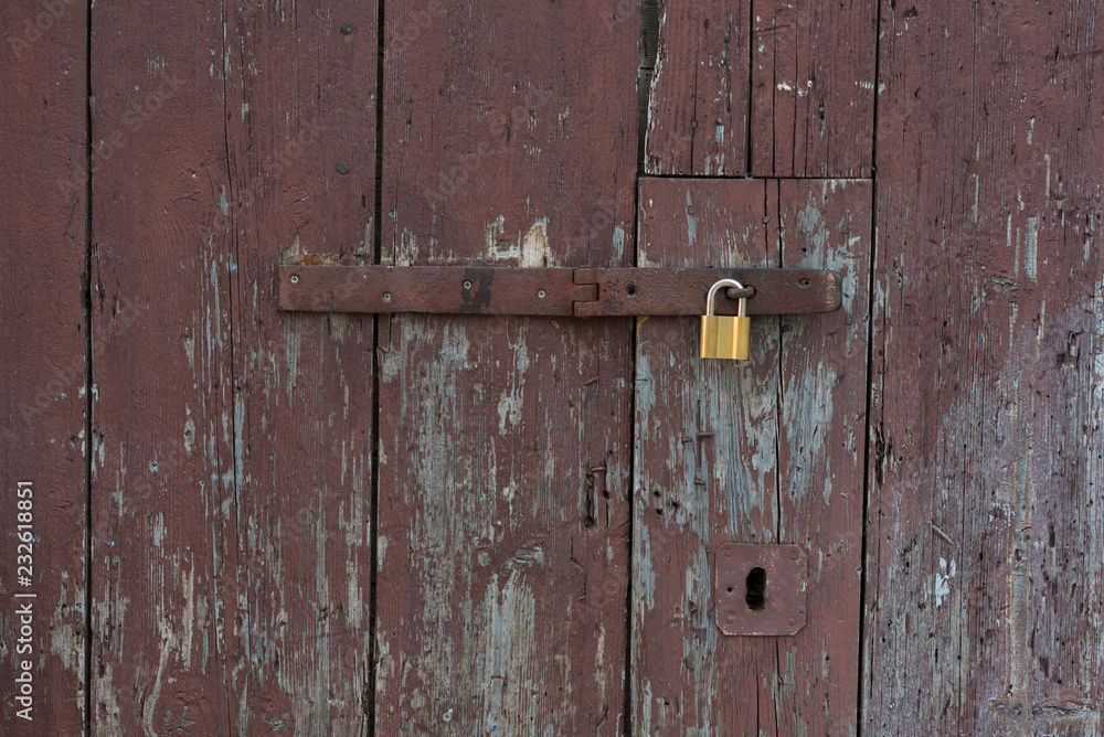 Old wooden doors locked with metal yellow lock. New yellow lock on old brown doors.