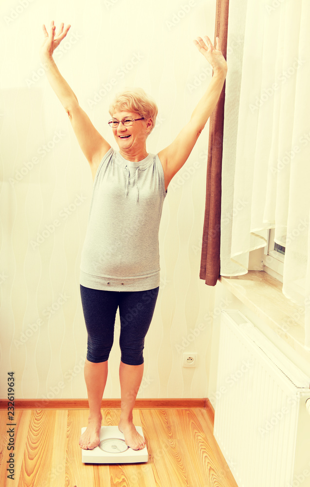 Happy senior woman standing on weight scale in living room Happy senior woman standing on weight scale in living room