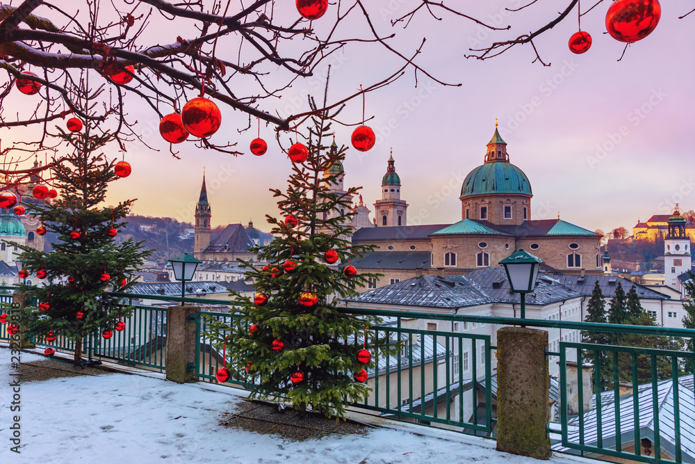 Fototapeta premium Piękny widok na zabytkowe miasto Salzburg ze słynną katedrą w Salzburgu w zimie, Austria. Choinki z czerwonymi bombkami na tle zimy Salzburg.