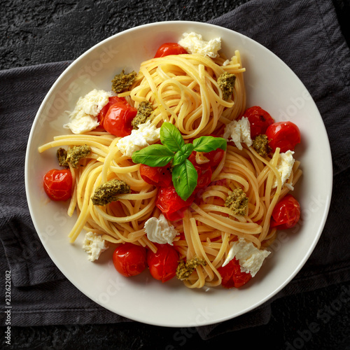 Pasta with green pesto sauce, roasted cherry tomatoes and mozzarella cheese in white plate on dark rustic background