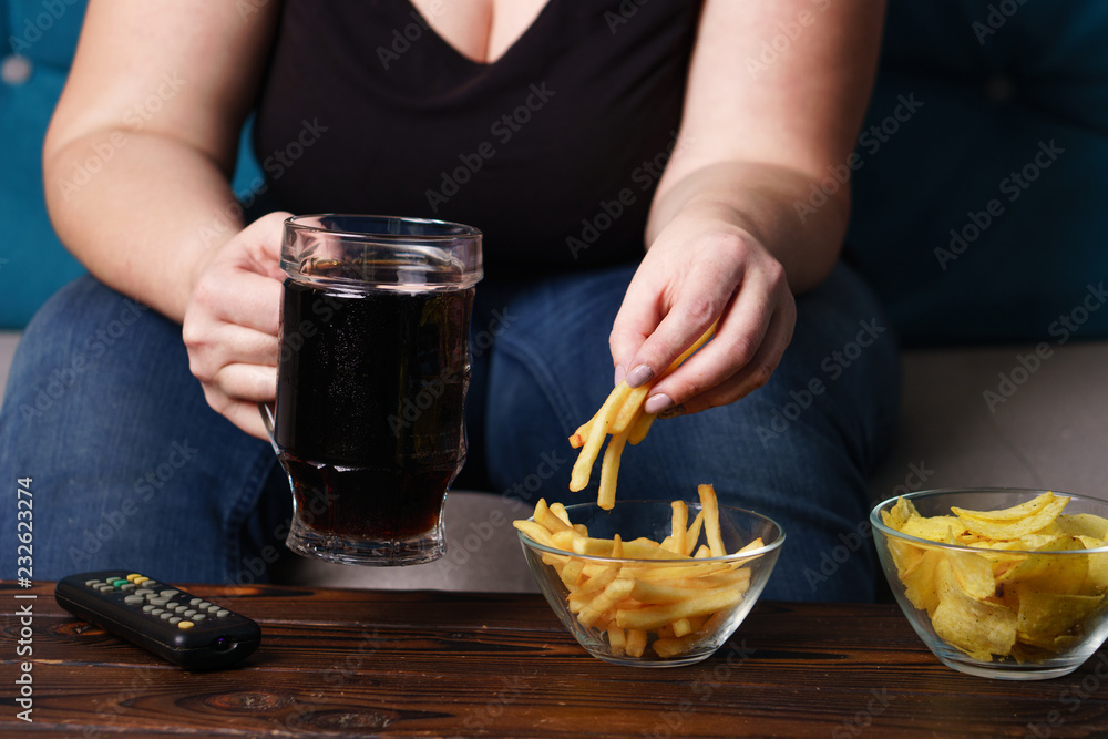 sedentary lifestyle, bad habits, food addiction, overeating, eating disorders. fat overweight woman sitting on the sofa with junk food and tv remote. depression, laziness problem eating sedentary lifestyle, bad habits, food addiction, overeating, eating disorders. fat overweight woman sitting on the sofa with junk food and tv remote. depression, laziness problem eating