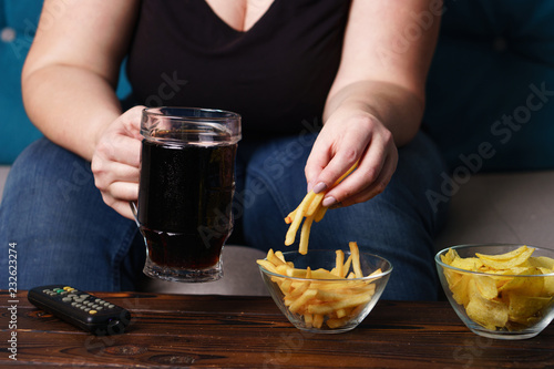 sedentary lifestyle, bad habits, food addiction, overeating, eating disorders. fat overweight woman sitting on the sofa with junk food and tv remote. depression, laziness problem eating