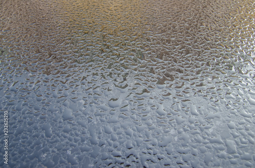 drops of rain on the hood of a black car with a reflection of the sky