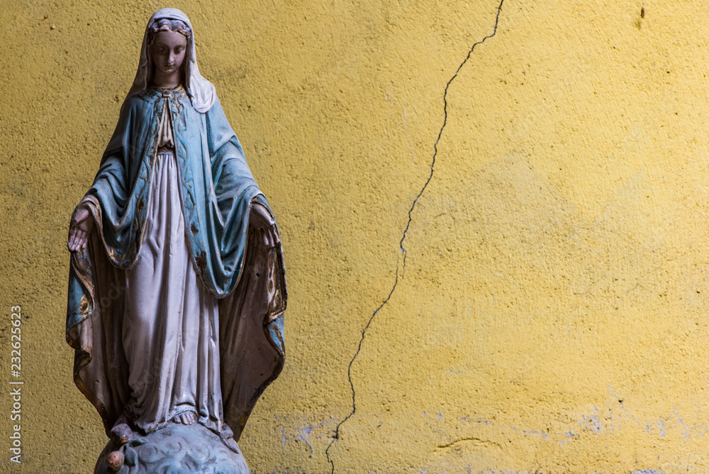 Old Virgin Mary statue, cracked wall background