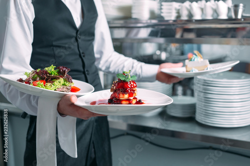 Waiter serving in motion on duty in restaurant. The waiter carries dishes photo