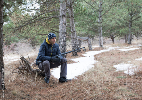 caucasian man is resting in winter forest with a shotgun. Hunting with a shotgun