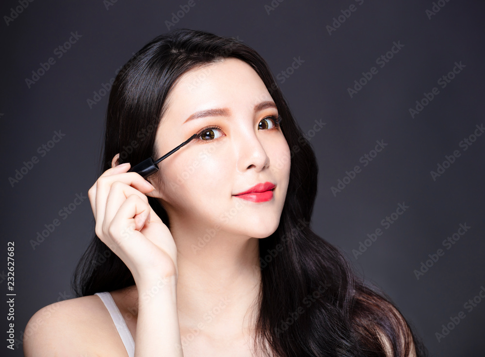 young woman applying black eye mascara to her eyelashes
