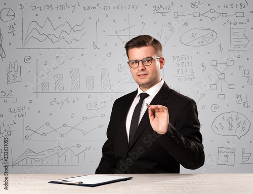 Young handsome businessman sitting at a desk with white charts behind him