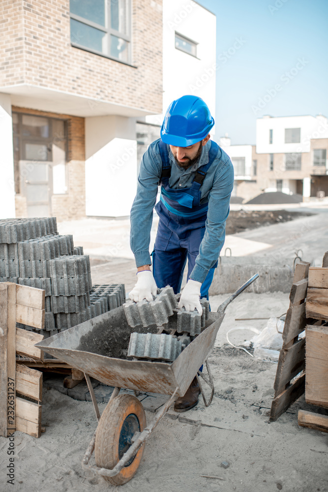 Builder loading paving tiles into the pushcart standing on the construction site Builder loading paving tiles into the pushcart standing on the construction site