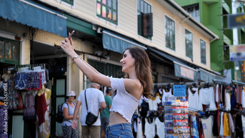 Beautiful young caucasian taking selfie in city centre are walking Khaosan Road walking street in evening at Bangkok, Thailand. Happy female traveler and tourist concept..