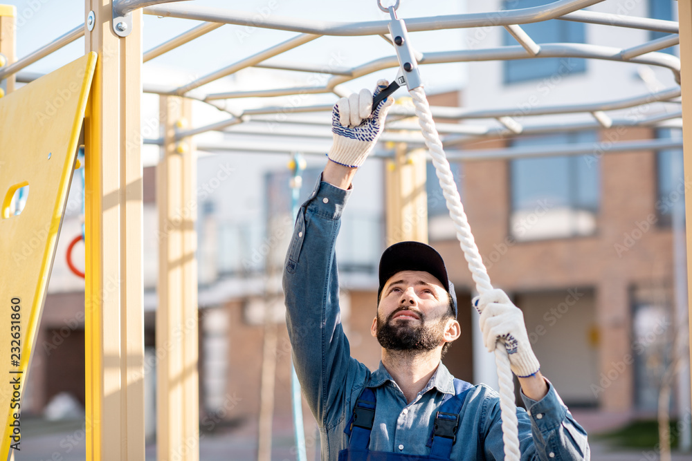 Handsome workman in uniform mounting rope for climbing on the playground outdoors Handsome workman in uniform mounting rope for climbing on the playground outdoors