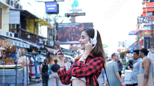 Beautiful young woman caucasian listening to music and walking street in evening at Bangkok, Thailand.
