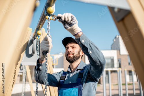 Photography Handsome workman in uniform mounting swing on the playground outdoors