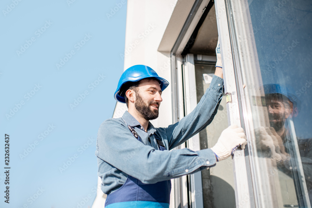 Workman in uniform mounting windows checking the level on the white building facade Workman in uniform mounting windows checking the level on the white building facade