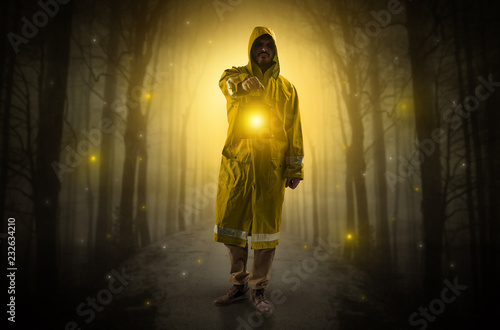 Man in raincoat coming from dark forest with glowing lantern in his hand concept  © ra2 studio