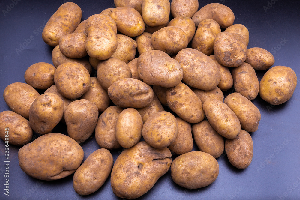 heap of fresh organic yellow unwashed potato stand out among many large background potatos in the market. Close-up texture. heap of fresh organic yellow unwashed potato stand out among many large background potatos in the market. Close-up texture.