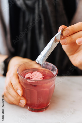 Unidentified person pouring pink medicine powder into a glass of water to dissolve