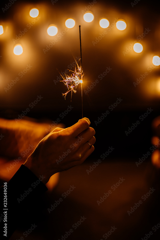 Sparkling Bengal fire in man hand on white background with yellow ballons numbers 2019. Christmas Holiday Concept