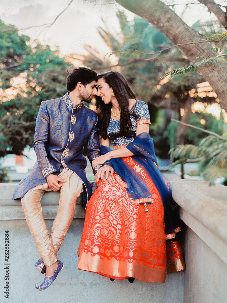 A loving couple smiling at each other sitting on a wall wearing ...