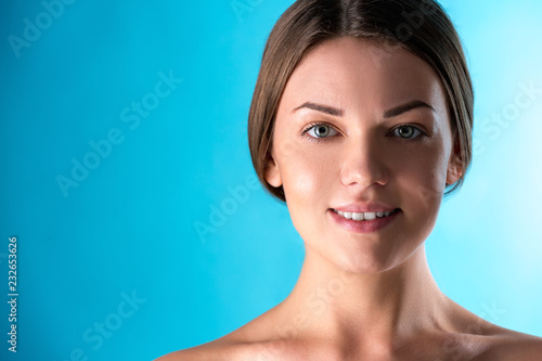 Beautiful Woman Face. Beauty Portrait of young woman brunette smiling on blue background. Perfect Fresh Skin. Youth and Skin Care Concept.