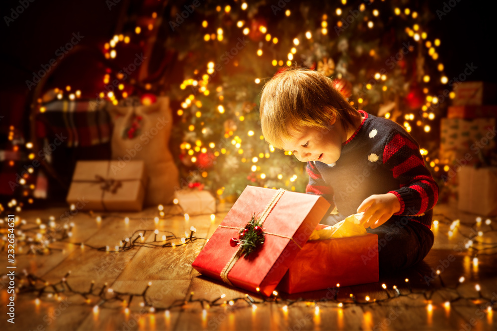 Christmas Child Open Present Gift, Happy Baby Boy looking to Magic Light in Box, Kid sitting front of Xmas Tree - obrazy, fototapety, plakaty 