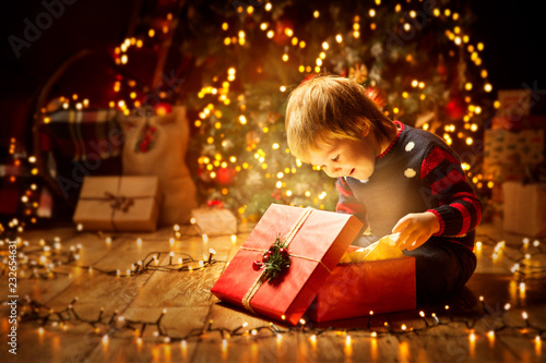 Christmas Child Open Present Gift, Happy Baby Boy looking to Magic Light in Box, Kid sitting front of Xmas Tree