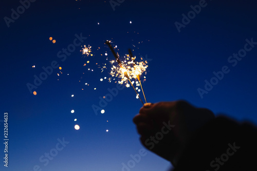 Female hand holding sparkler against a dark sky photo