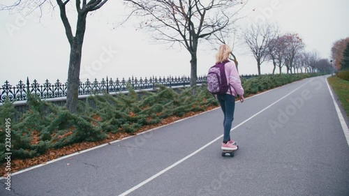 Young pretty beautiful blond hipster woman in pink windstopper having fun riding skateboard longboard downhill on beautiful road in slow motion photo