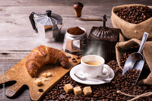 on the rustic wooden table a cup of hot coffee with croissant, a vintage coffee grinder, an Italian moka and coffee beans. High angle view photo