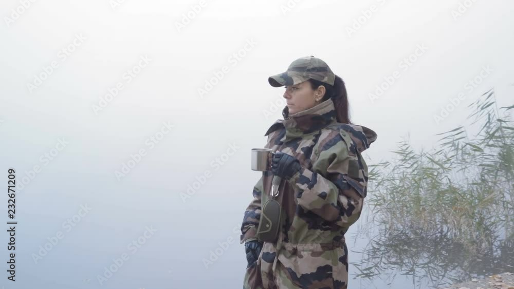 Beautiful Military Woman in Army Camouflage Drinks Hot Tea Holding a Metal Mug on the Background of the River in the Fog on an Autumn Morning Beautiful Military Woman in Army Camouflage Drinks Hot Tea Holding a Metal Mug on the Background of the River in the Fog on an Autumn Morning
