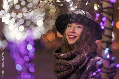 Young girl standing in front of christmas tree lights at night with snowflakes falling, snowing © qunica.com