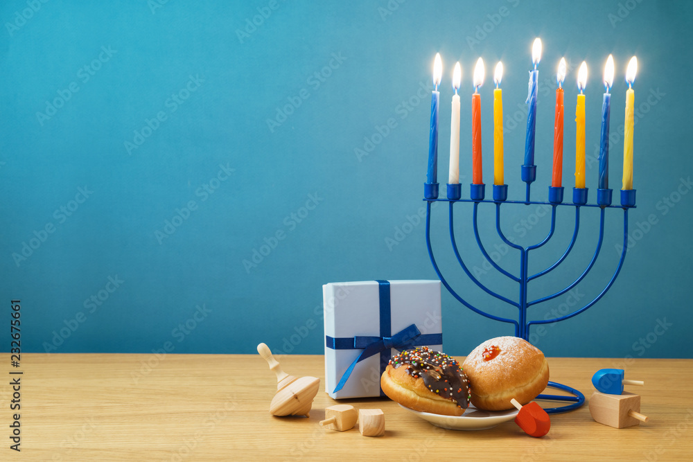 Naklejka premium Jewish holiday Hanukkah background with menorah, sufganiyot, gift box and spinning top on wooden table