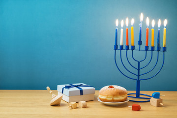 Jewish holiday Hanukkah background with menorah, sufganiyot, gift box and spinning top on wooden table