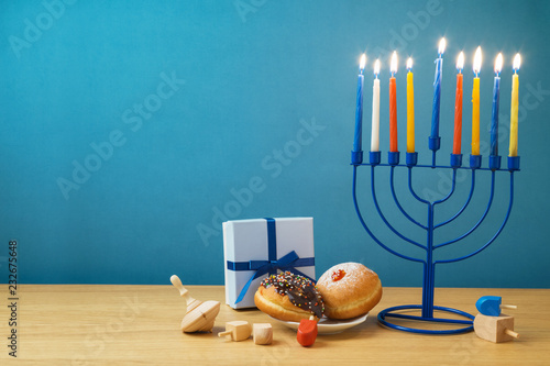 Jewish holiday Hanukkah background with menorah, sufganiyot, gift box and spinning top on wooden table