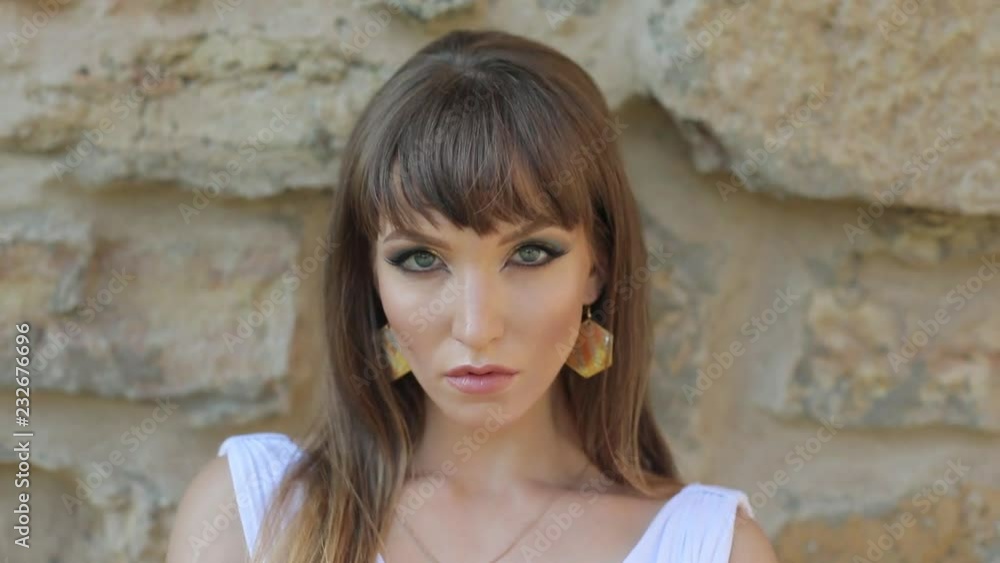 A girl with Arabic makeup walks in a white dress against an ancient stone wall. Looks at the camera and poses. A girl with Arabic makeup walks in a white dress against an ancient stone wall. Looks at the camera and poses.