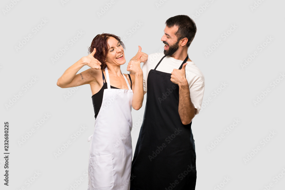 Couple of cooks giving a thumbs up gesture and smiling because has had success on grey background Couple of cooks giving a thumbs up gesture and smiling because has had success on grey background