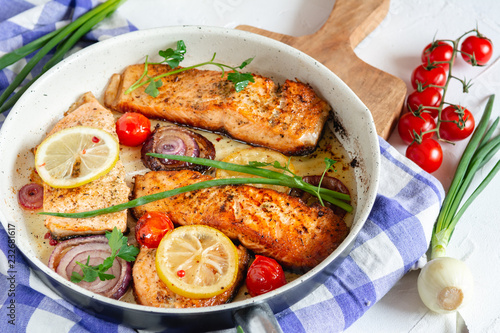 Salmon fried in a pan with onions, lemon and cherry tomatoes