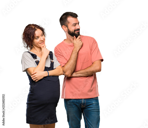 Couple with pregnant woman looking to the side with the hand on the chin on isolated white background