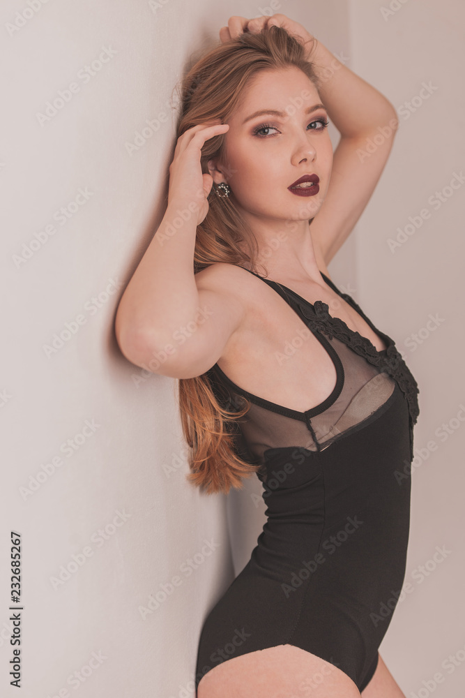 Fototapeta premium Boudoir photography of a beautiful woman standing near white wall in black body