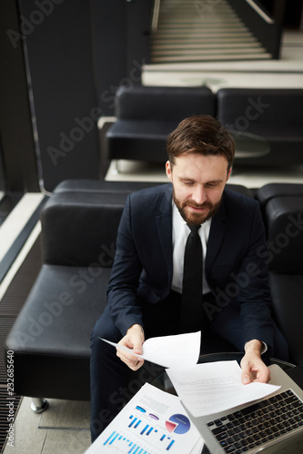 Young attractive and elegant businessman reading financial documents over laptop © pressmaster