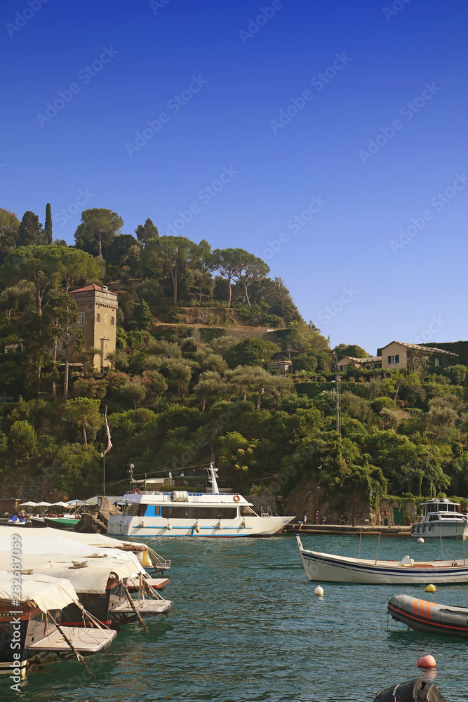 Obraz premium PORTOFINO, ITALY - suggestive view of Portofino harbor with an antique tower among lush Mediterranean vegetation and the boats moored