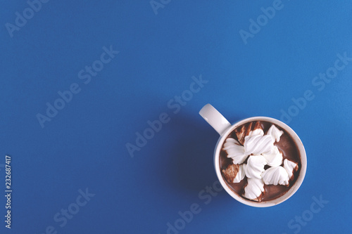 Hot chocolate with marshmallow candies on blue paper background. Top view. Copy space. Toned