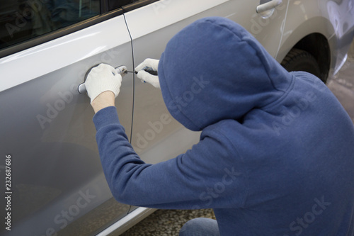 The hijacker tries to break into the car with a lock pick. Car thief, car theft. photo