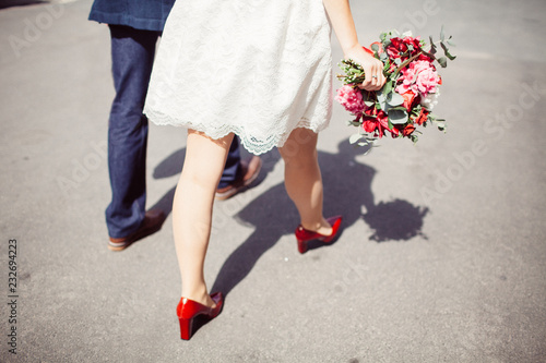 The legs of the bride with a bouquet and the groom walk during a sunny day photo